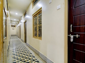 A corridor with patterned flooring, a wooden door with a metal handle, and a window with decorative bars. - Hotel O Gajraj (Guwahati)