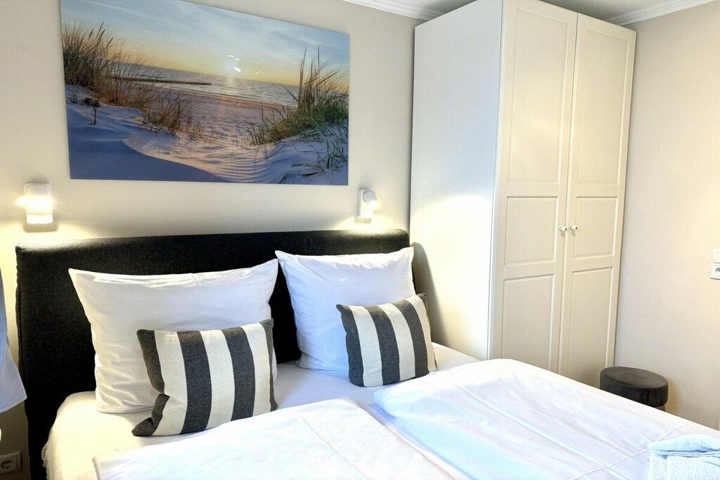 A hotel room with a bed, a painting of a beach scene, a wardrobe, and bedside lamps.