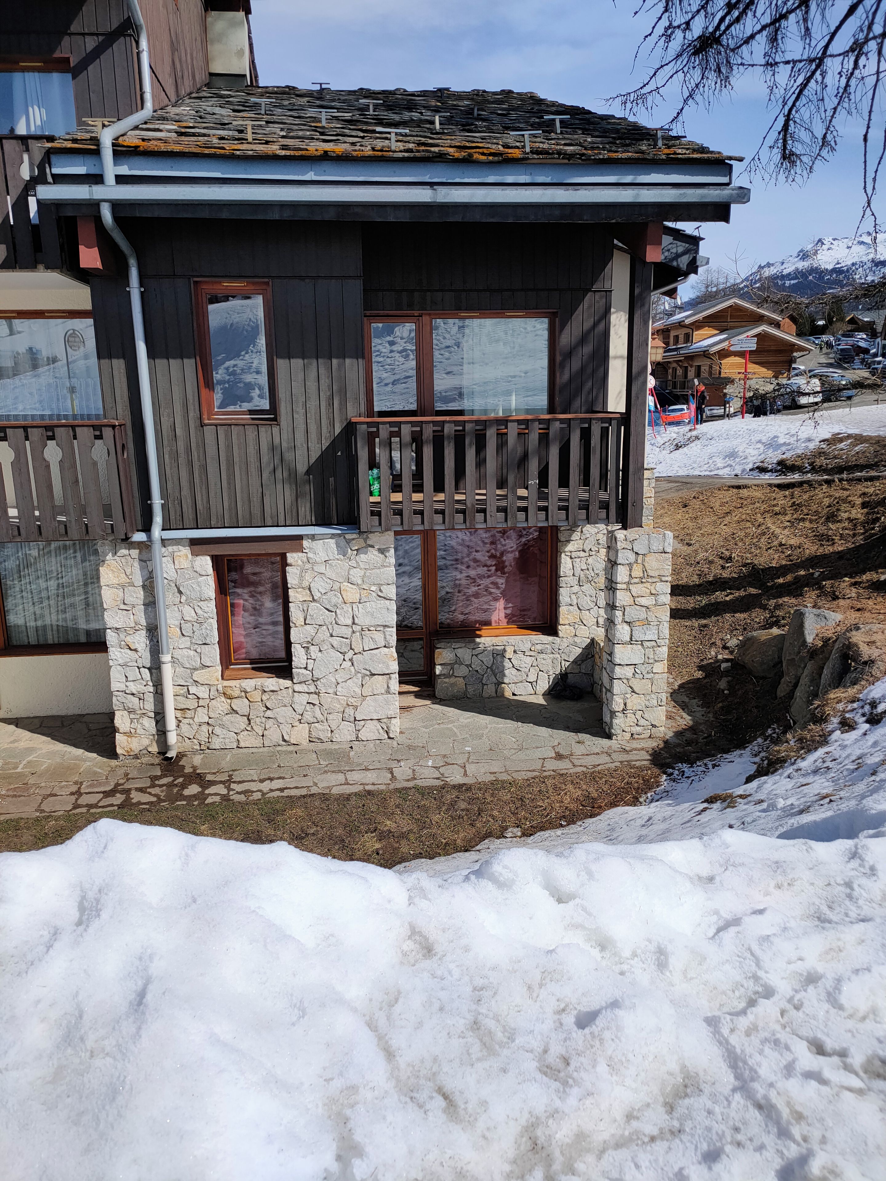 A wooden cabin with stone foundations, a balcony, and a view of a snowy landscape.