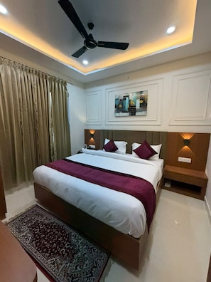 A hotel room with a bed, a ceiling fan, recessed lighting, a nightstand, and a rug. - VM Anandam (Varanasi)