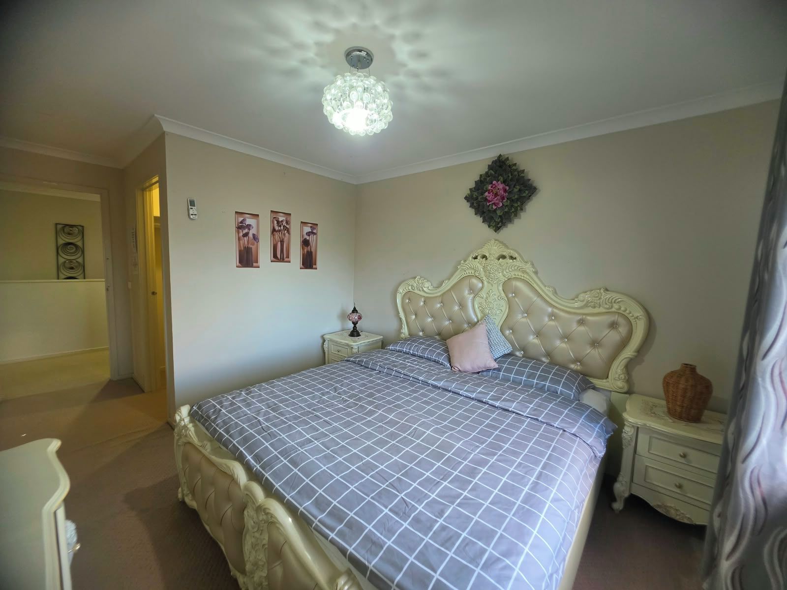 A bedroom with a large bed, a nightstand, a wall-mounted light fixture, and a door leading to another room.