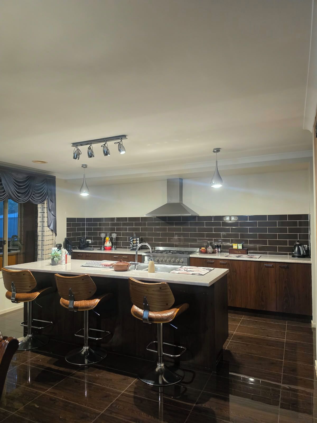 A modern kitchen with a central island, bar stools, a stove, and a large window.