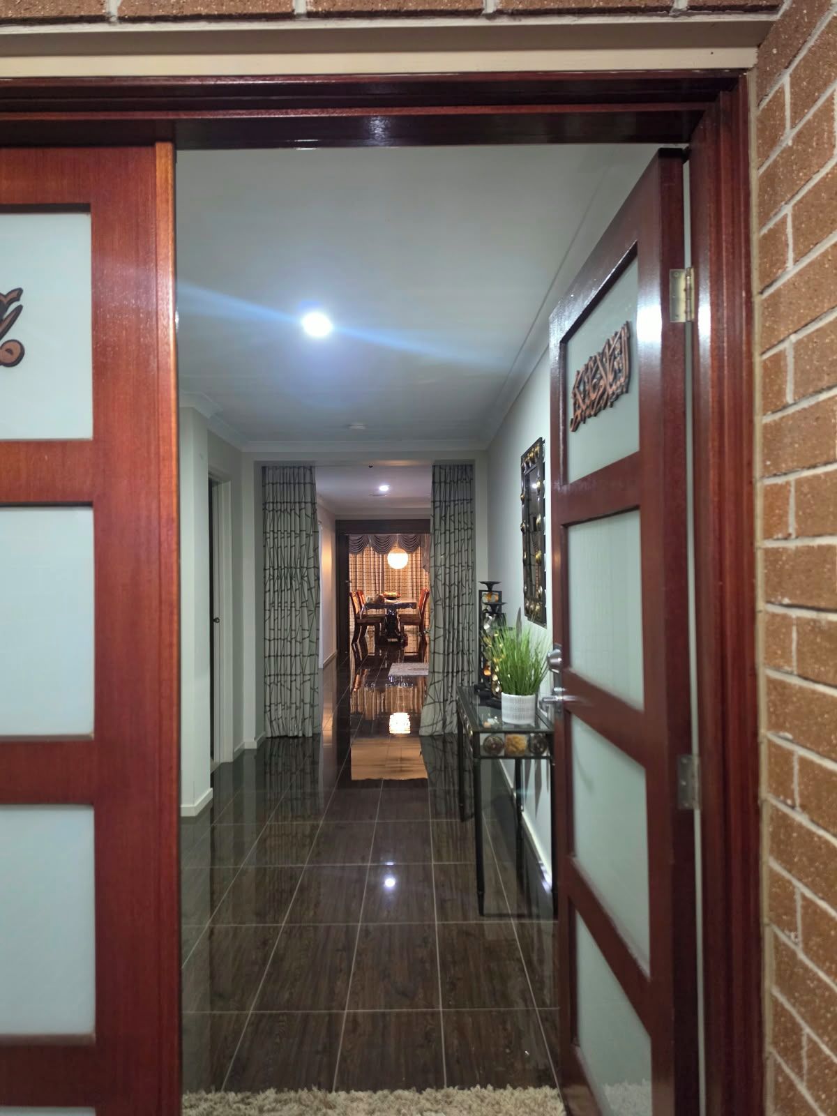 A hallway with a wooden door, a dining area with a table and chairs, and a small plant on a console table.