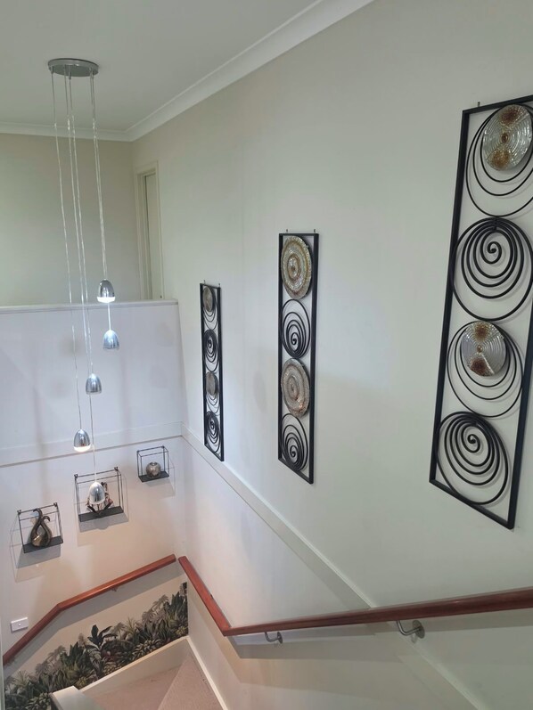 A staircase with a handrail, a wall with decorative metal art pieces, and a hanging light fixture.