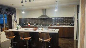 A modern kitchen with a central island, bar stools, a gas stove, and a backsplash.