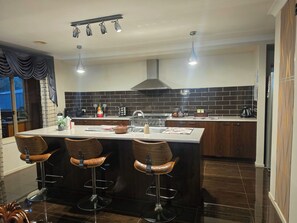 A modern kitchen with a central island, bar stools, a gas stove, and a backsplash.