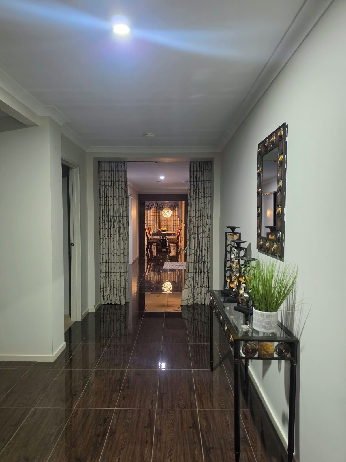 A hallway with a dark wood floor, a table with a potted plant, and a mirror on the wall.