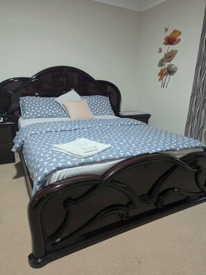 A bed with a geometric patterned bedspread, a wooden headboard, and a wall with a floral mural.