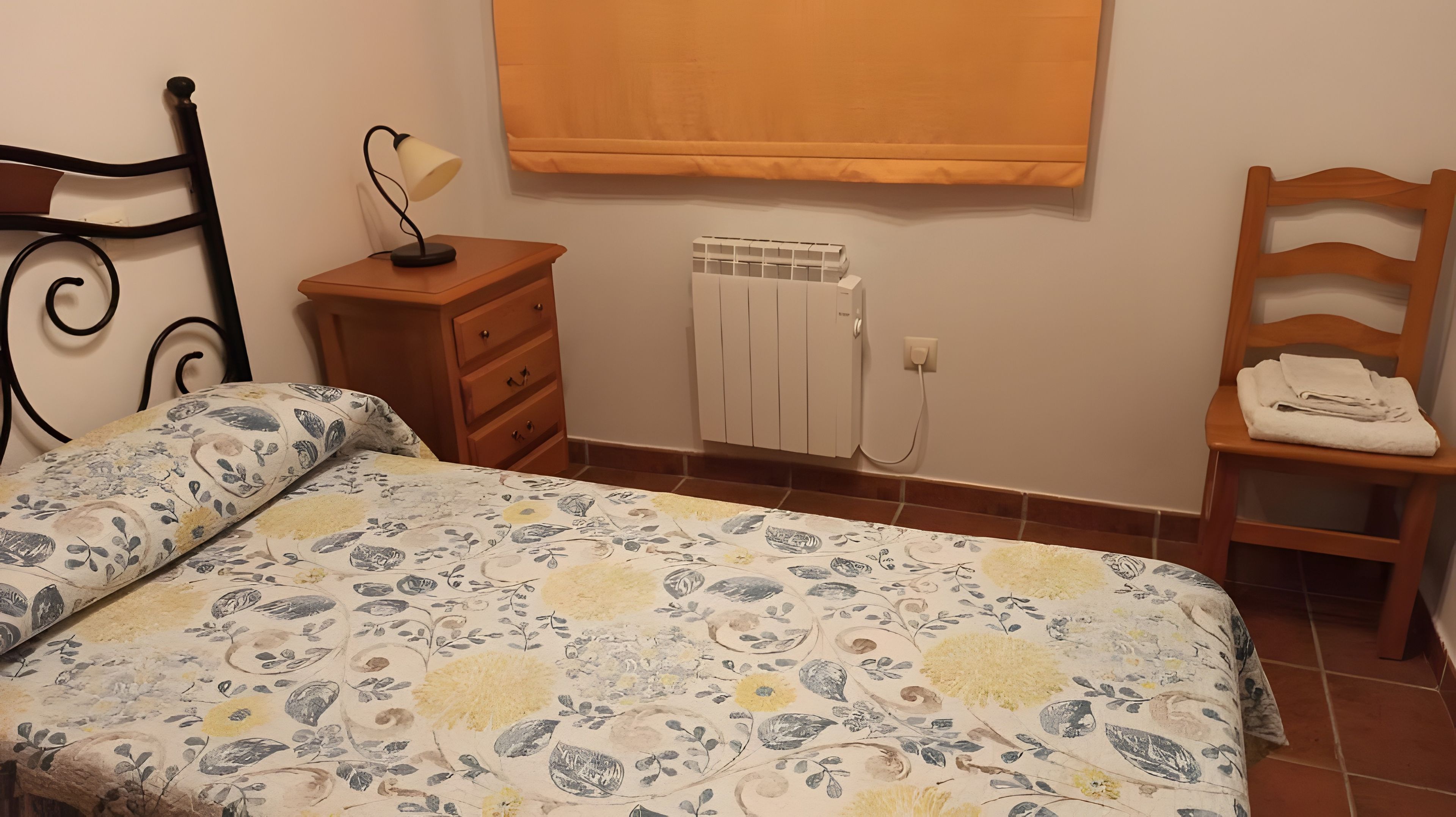 A bedroom with a bed, a nightstand, a radiator, and a chair.