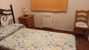 Un dormitorio con cama, mesita de noche, radiador y una silla.