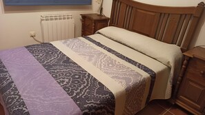 Quarto com cama, cabeceira de madeira, mesa de cabeceira e radiador.