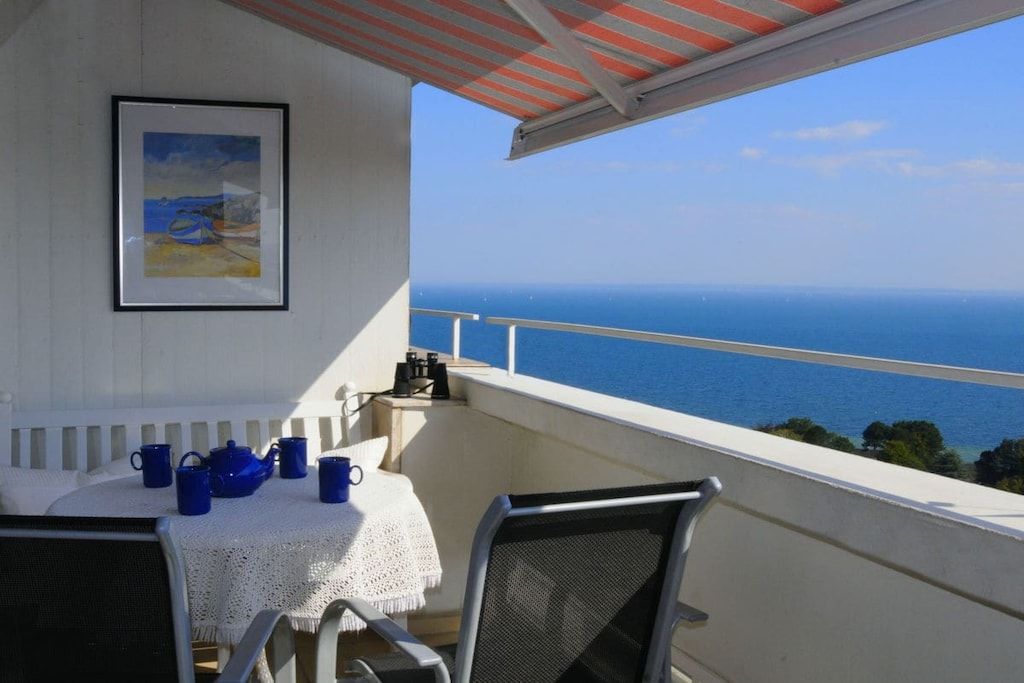 Un balcon avec une table dressée pour deux personnes, un tableau encadré au mur et une vue sur la mer.