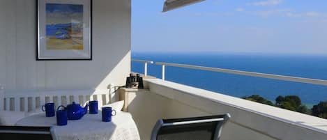 A balcony with a table set for two, a framed picture on the wall, and a view of the sea.