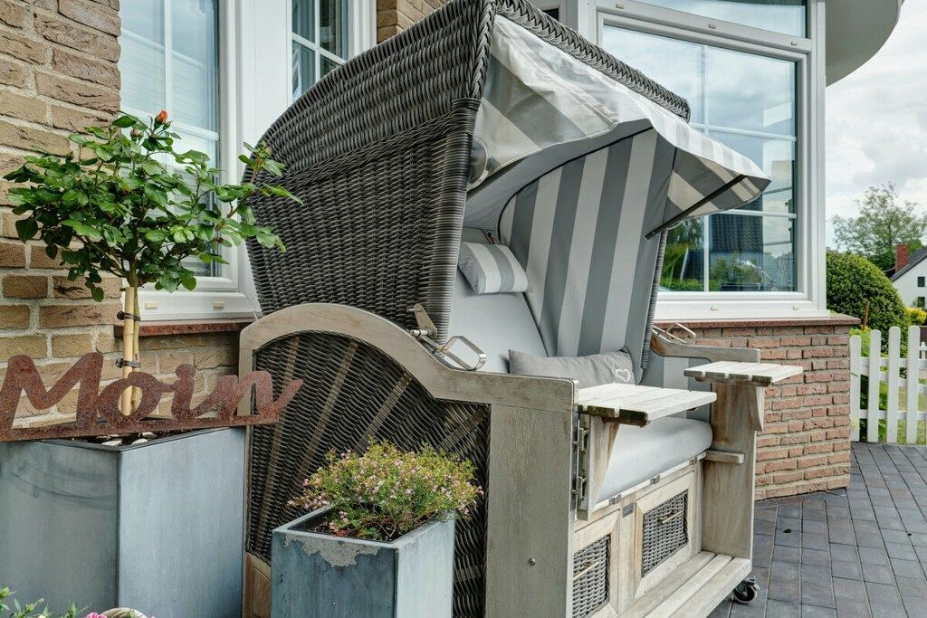 Un área de estar al aire libre con mobiliario de mimbre, una parrilla incorporada, una planta en maceta y un letrero con la palabra 'Moin'.