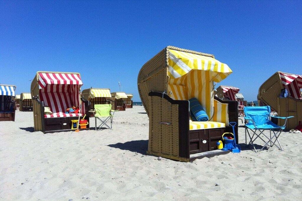 Des cabanes de plage dotées d’auvents à rayures, certaines avec des coussins et des chaises, et un ciel d’un bleu éclatant.