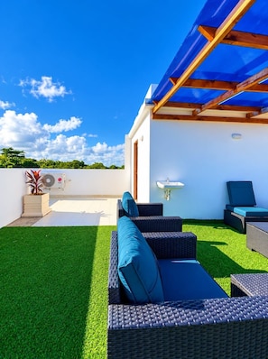 A rooftop patio with artificial grass, wicker furniture, a blue canopy, and a white wall with a sink. - Modern Comfort Villa  (Mombasa)