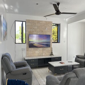 A modern living room with a stone accent wall, a flat-screen TV, grey sofas, and a ceiling fan. - Modern Comfort Villa  (Mombasa)
