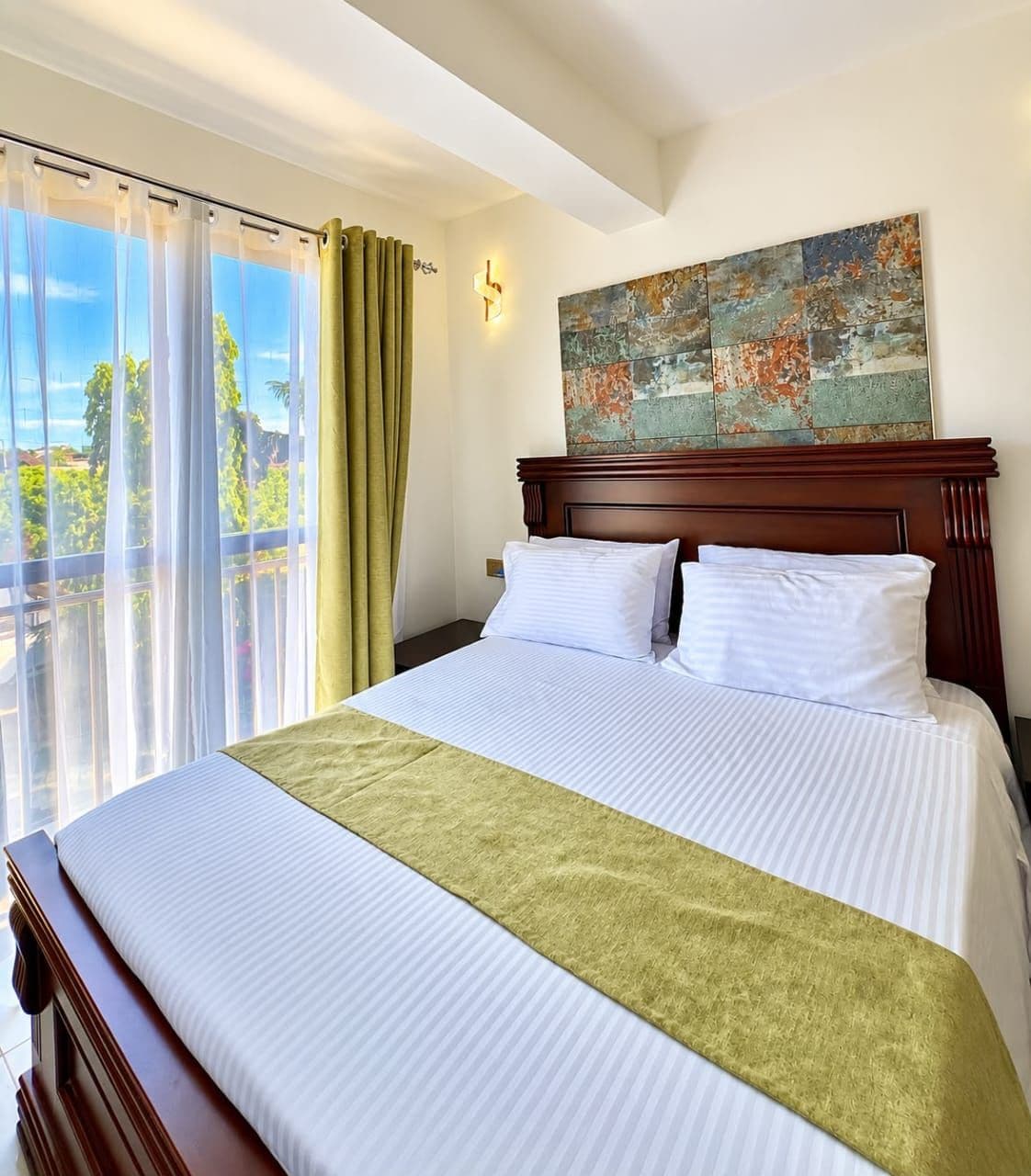 Une chambre d’hôtel avec un grand lit, une vue sur l’extérieur et un tableau au mur.