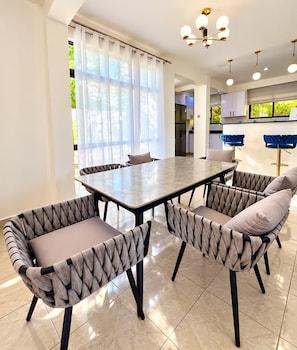 A dining area with a rectangular table and six upholstered chairs with a braided pattern. - Modern Comfort Villa  (Mombasa)