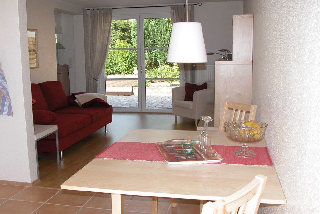 Un comedor con una mesa, sillas, un sofá rojo y vistas a un patio exterior a través de un ventanal.