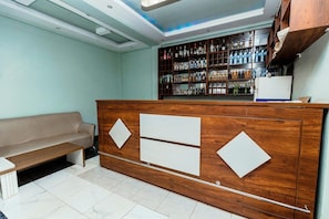 A reception area with a wooden counter, a sofa, and a wall-mounted liquor shelf. - Hulcity Gold Hotel (Kampala)