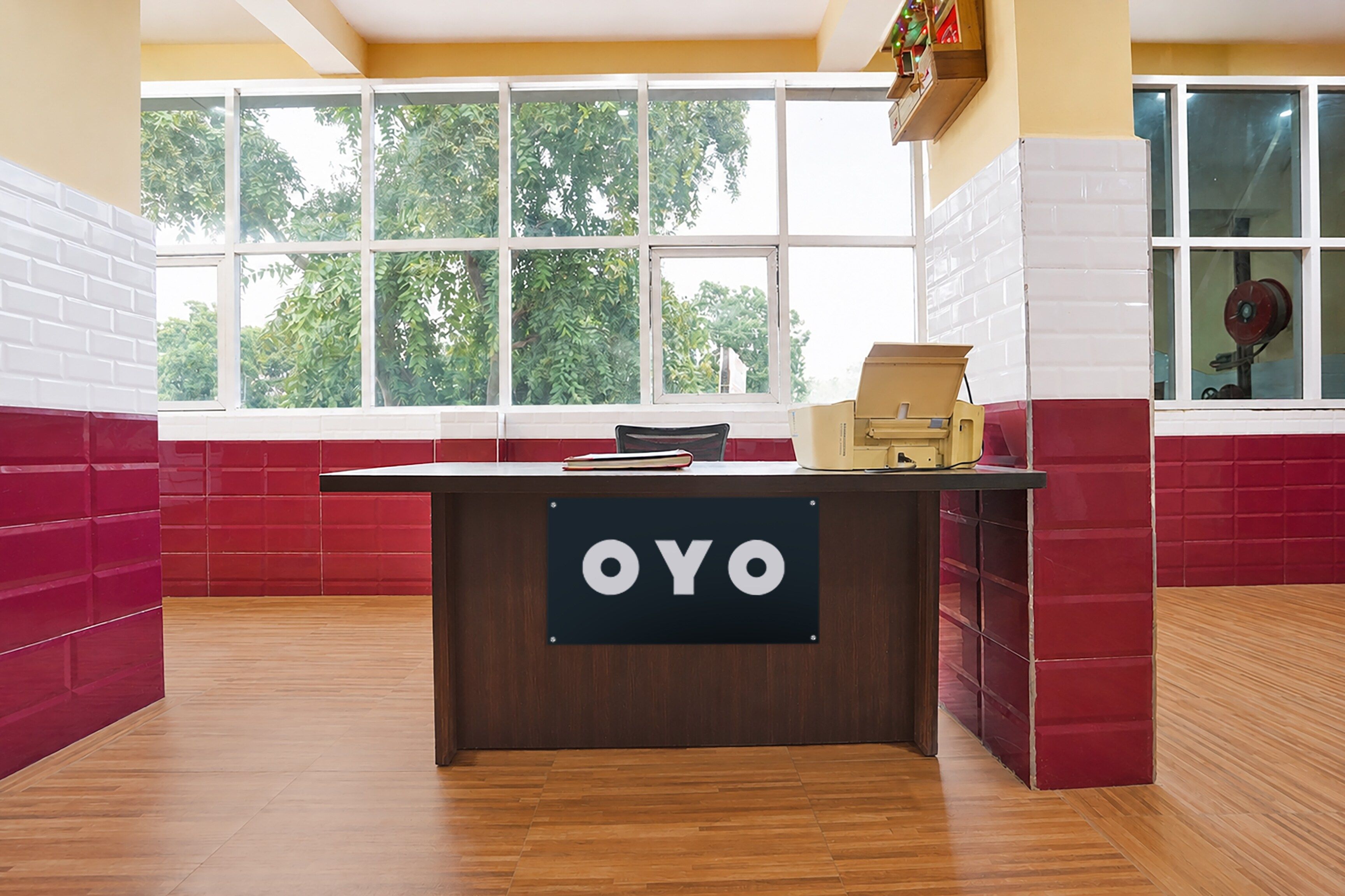 A reception desk with a sign reading 'OYO' in a room with red and white walls, large windows, and a view of trees.