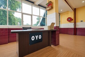 Una recepción con un cartel que dice 'OYO', en un interior moderno con un ventanal grande, un ventilador de pared y una pared con azulejos blancos y rojos.
