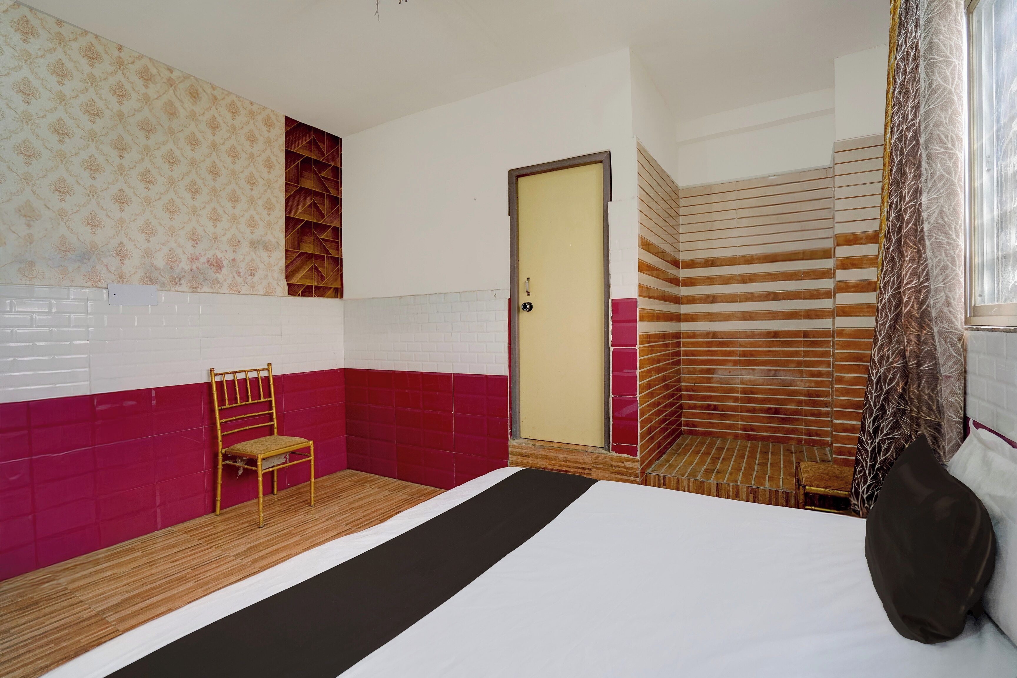 A hotel room with a bed, a chair, a door, and a window with curtains.