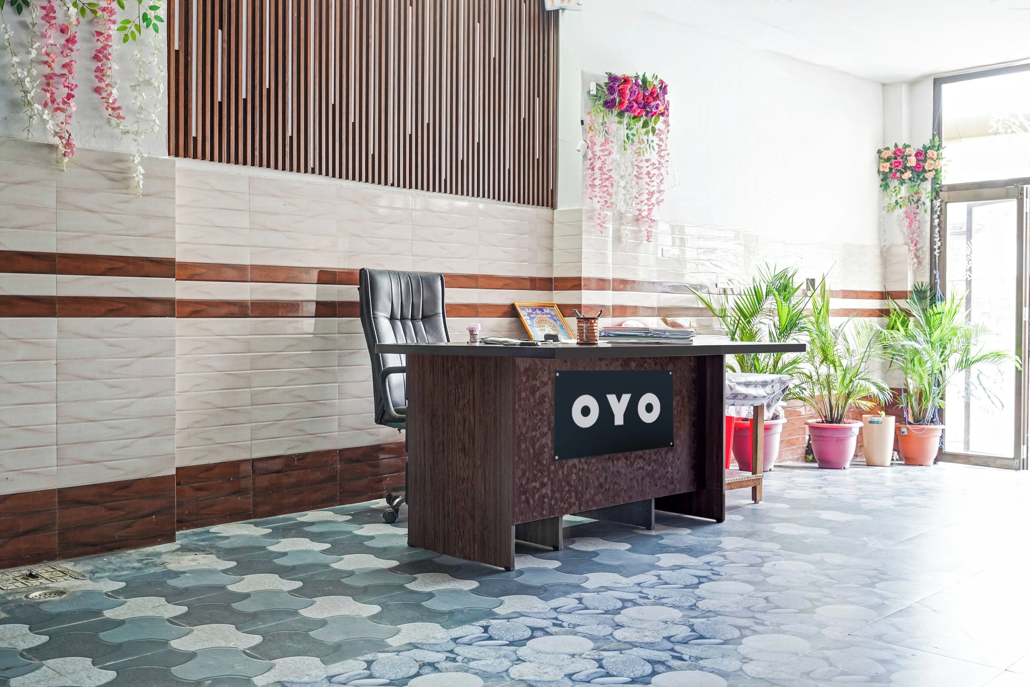 A reception desk with a sign reading 'OYO' in a modern lobby with patterned flooring and decorative plants.
