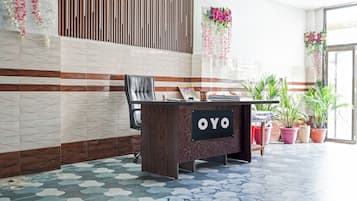 Un mostrador de recepción con un letrero que dice 'OYO' en un vestíbulo moderno con piso estampado y plantas decorativas.