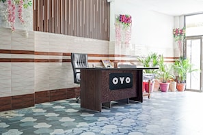 A reception desk with a sign reading 'OYO' in a modern lobby with patterned flooring and decorative plants. - Hotel O JS Palace (Gorakhpur)