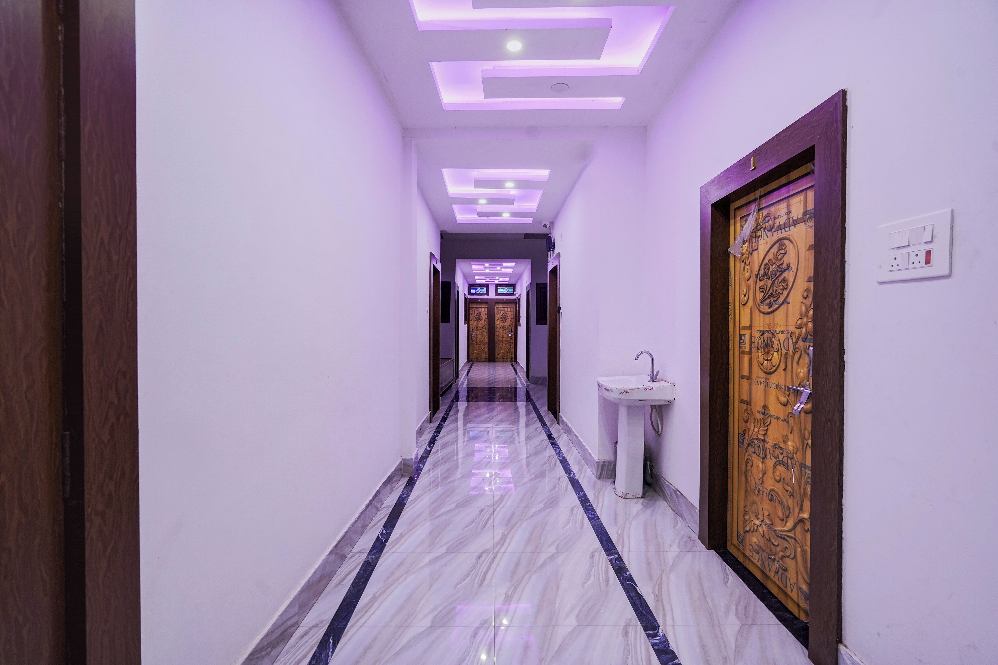 A hallway with a marble floor, a wooden door with a decorative panel, and a wall-mounted light switch.