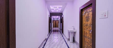 A hallway with a marble floor, a wooden door with a decorative panel, and a wall-mounted light switch.