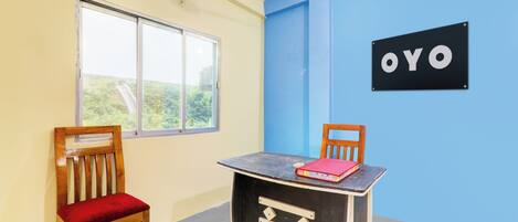 A room with a single window, a ceiling fan, a table with a red book, and a wall sign that reads 'OYO'.