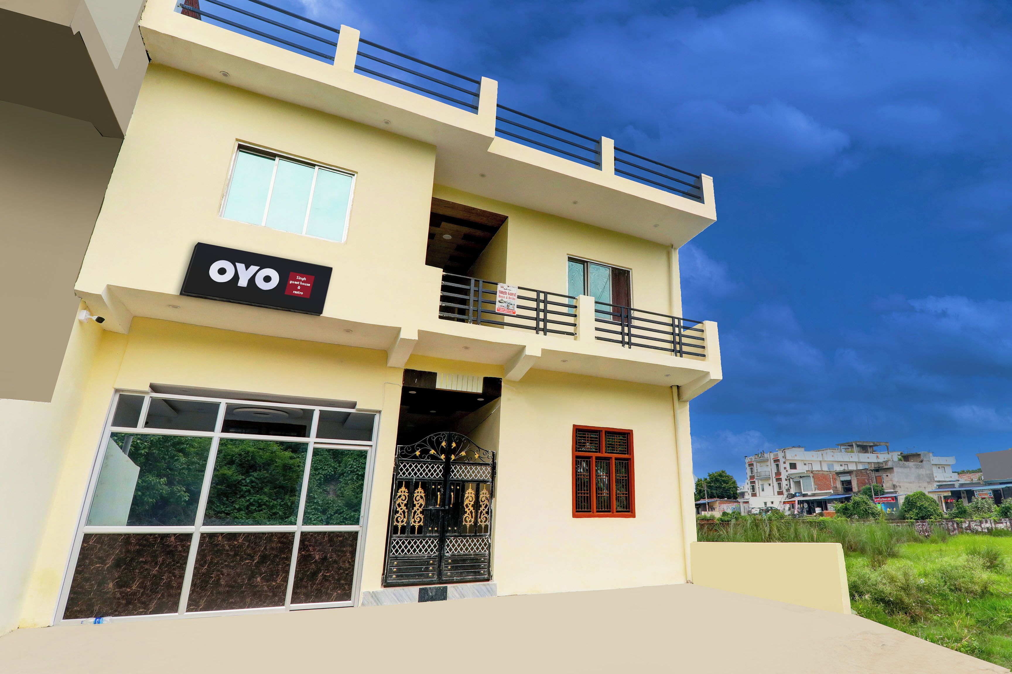 A two-story building with a flat roof, a balcony on the upper floor, and a sign indicating a guest house.