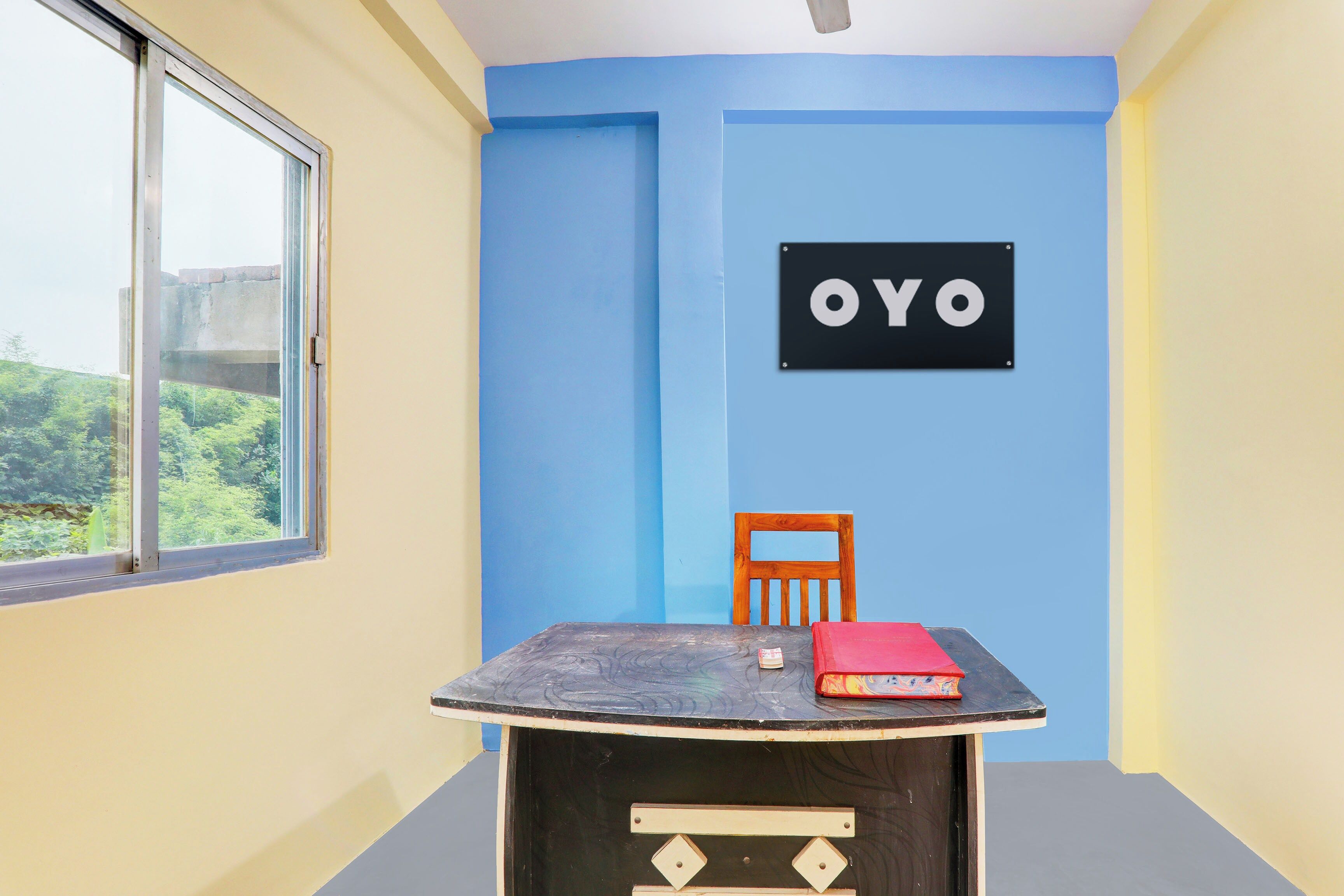 A room with a table, a chair, a window, and a wall with the word 'OYO' on it.
