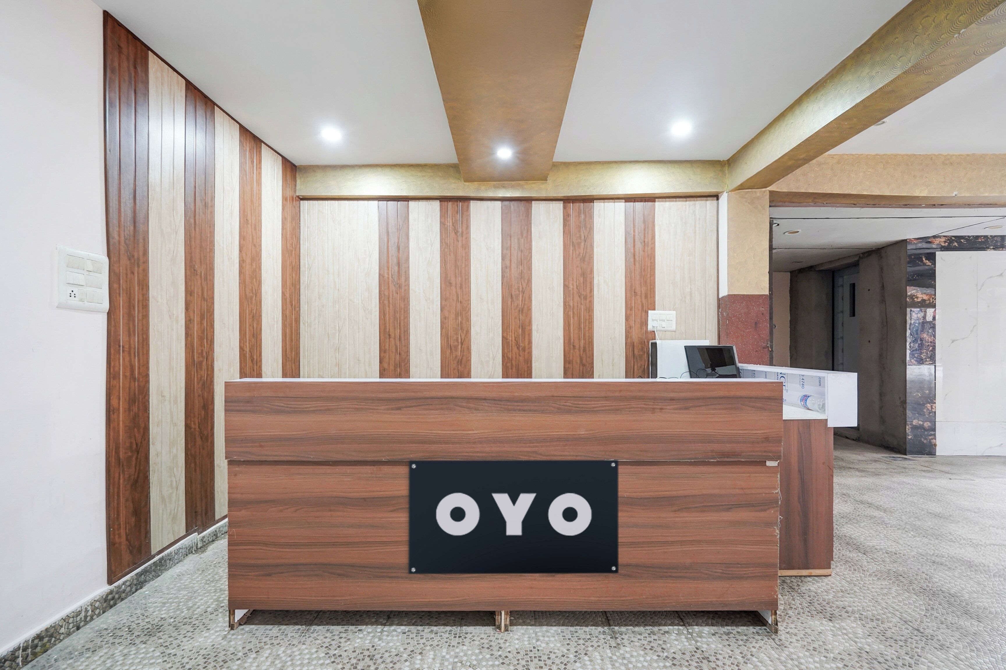 A reception desk with a sign reading 'OYO' in a modern interior with wooden paneling and a tiled floor.