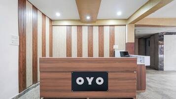 A reception desk with a sign reading 'OYO' in a modern interior with wooden paneling and a tiled floor.