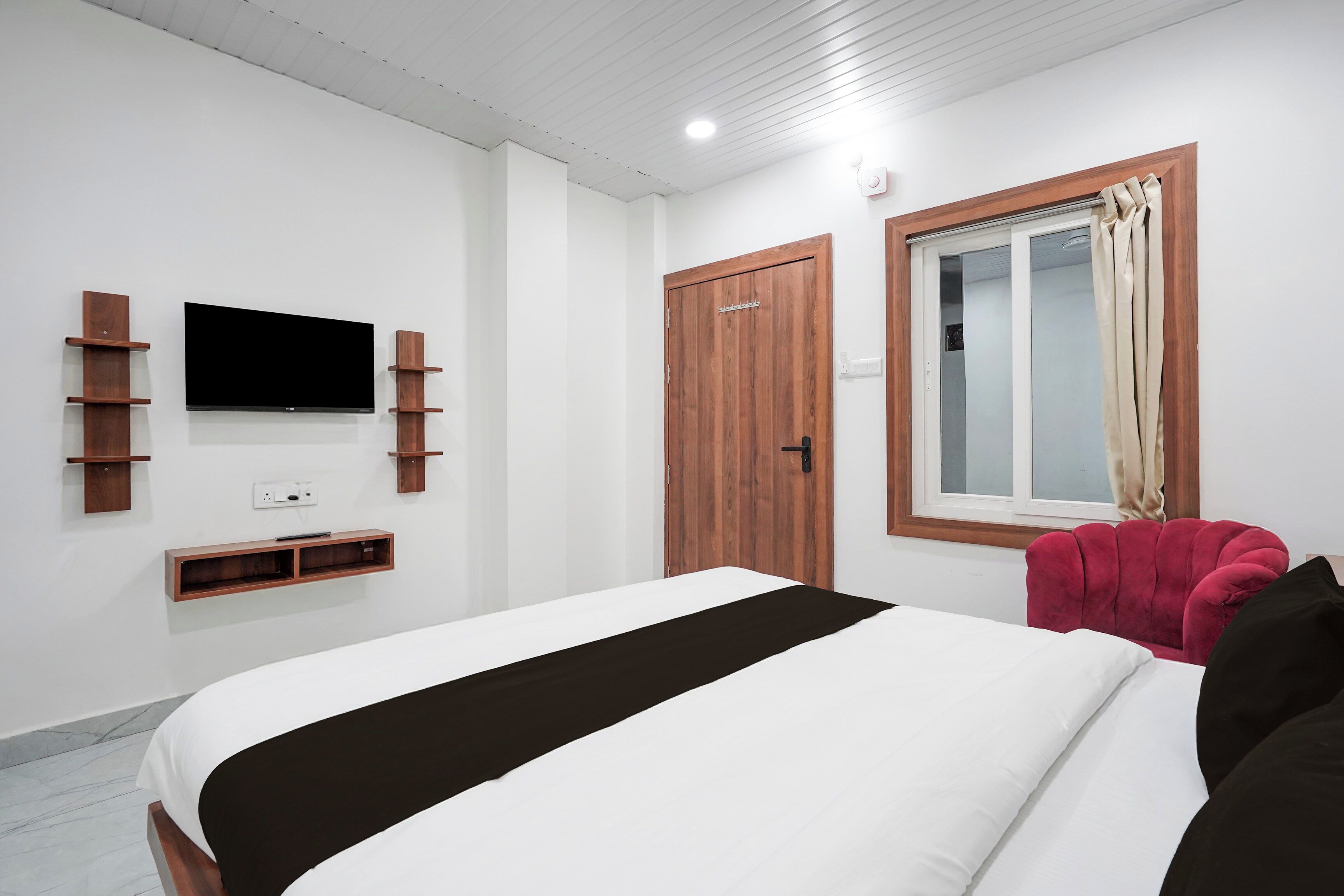 A bedroom with a bed, a TV mounted on the wall, a wardrobe, and a window with curtains.