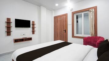 A bedroom with a bed, a TV mounted on the wall, a wardrobe, and a window with curtains.