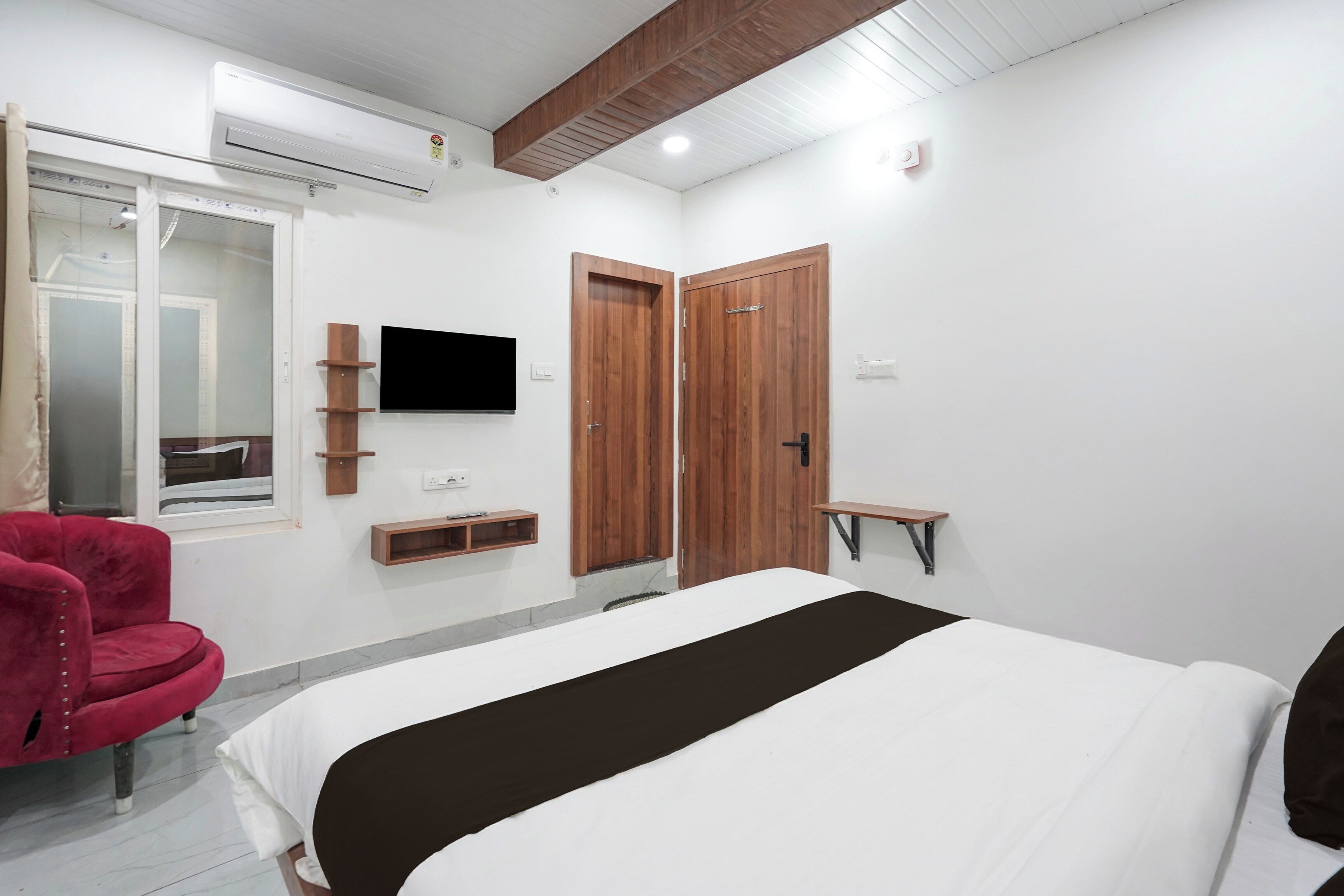 A bedroom with a bed, a TV, a wardrobe, and a red chair.