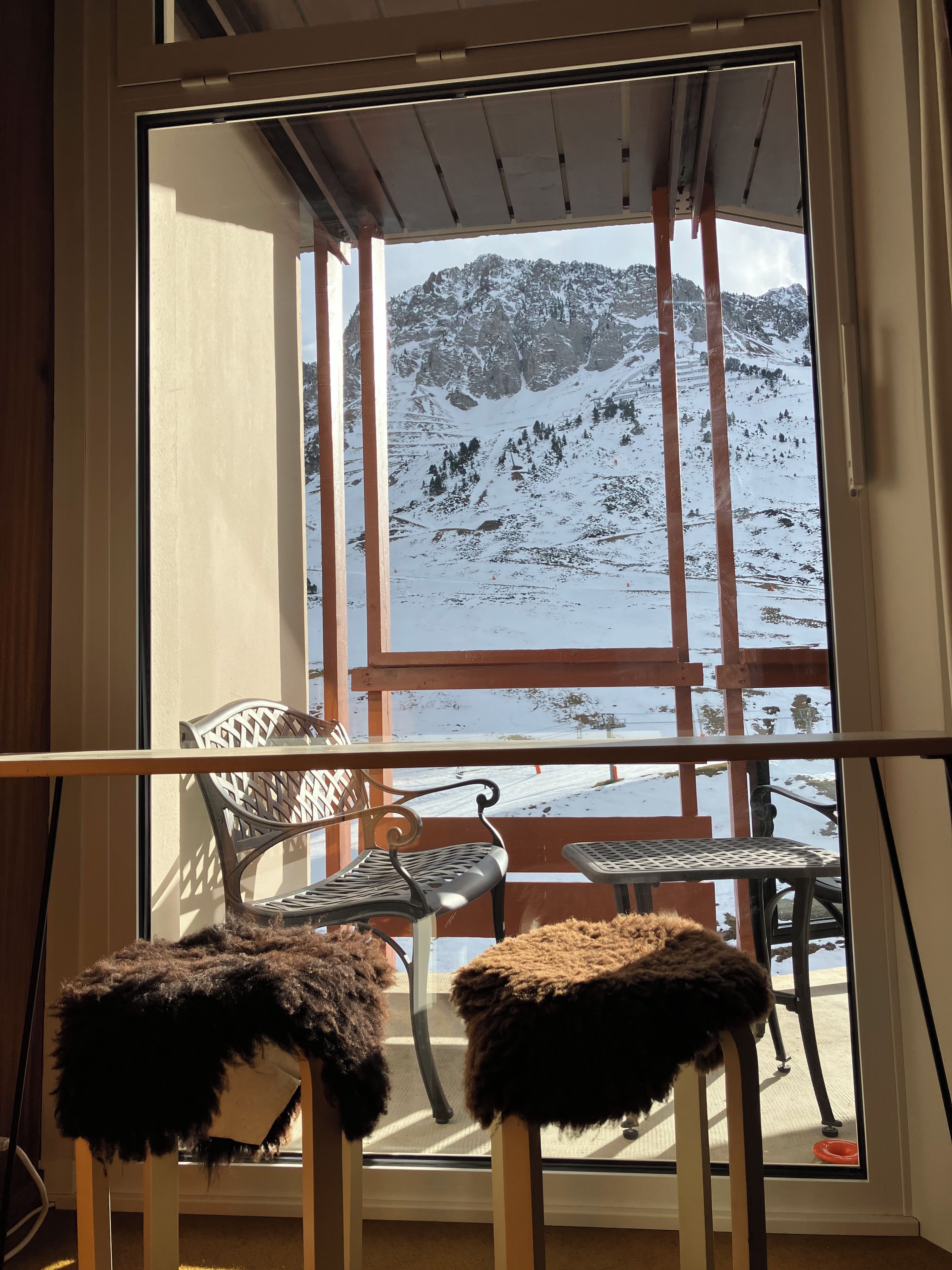 Una habitación con un ventanal grande que da a un paisaje nevado de montañas. Hay dos sillones con cojines de piel.