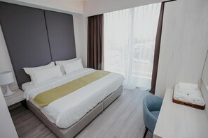 Quarto de hotel com uma cama, uma cadeira, mesa de cabeceira e janela com cortinas.