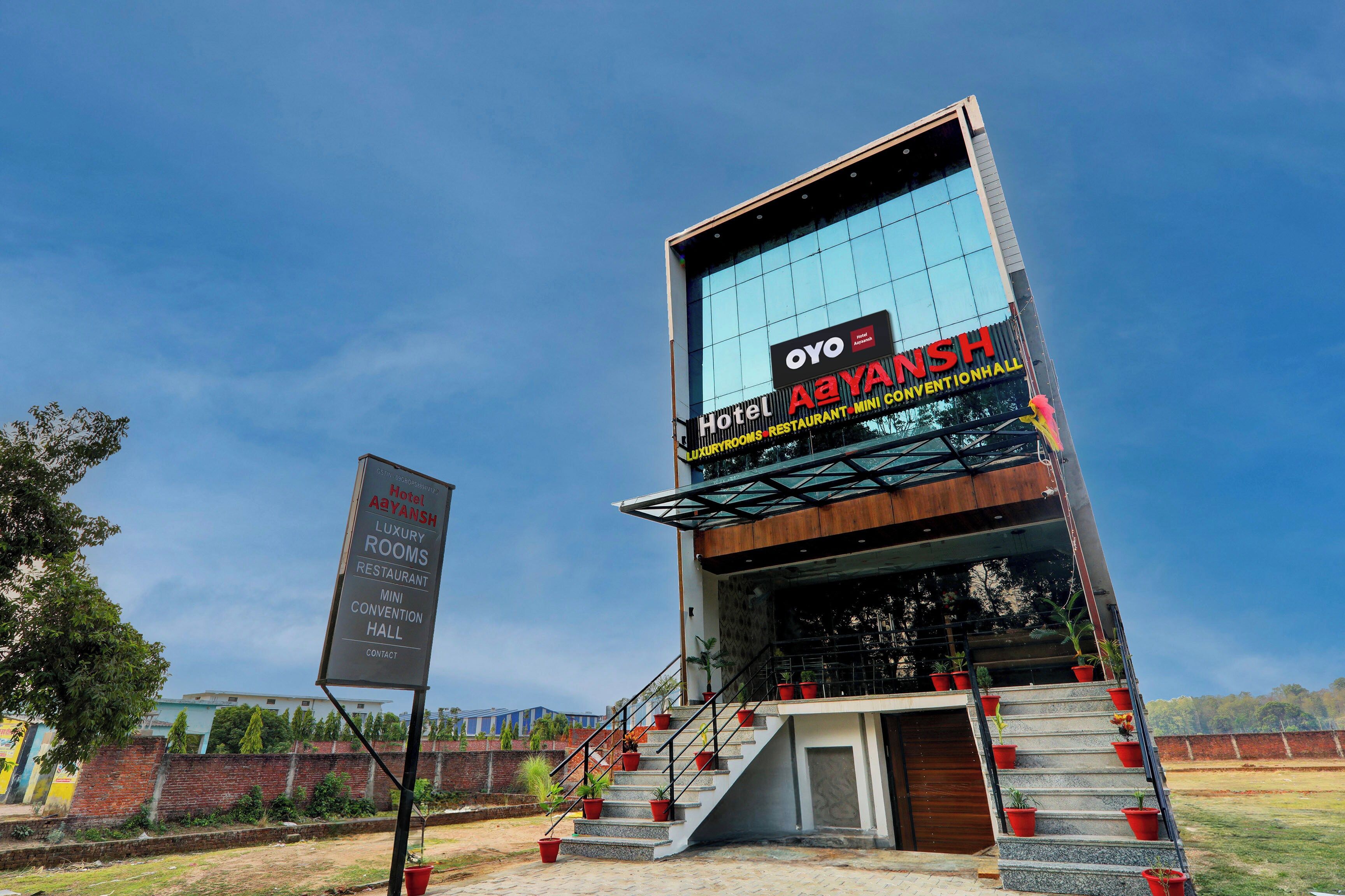 A modern hotel with a glass facade, a signboard, and a staircase with potted plants.