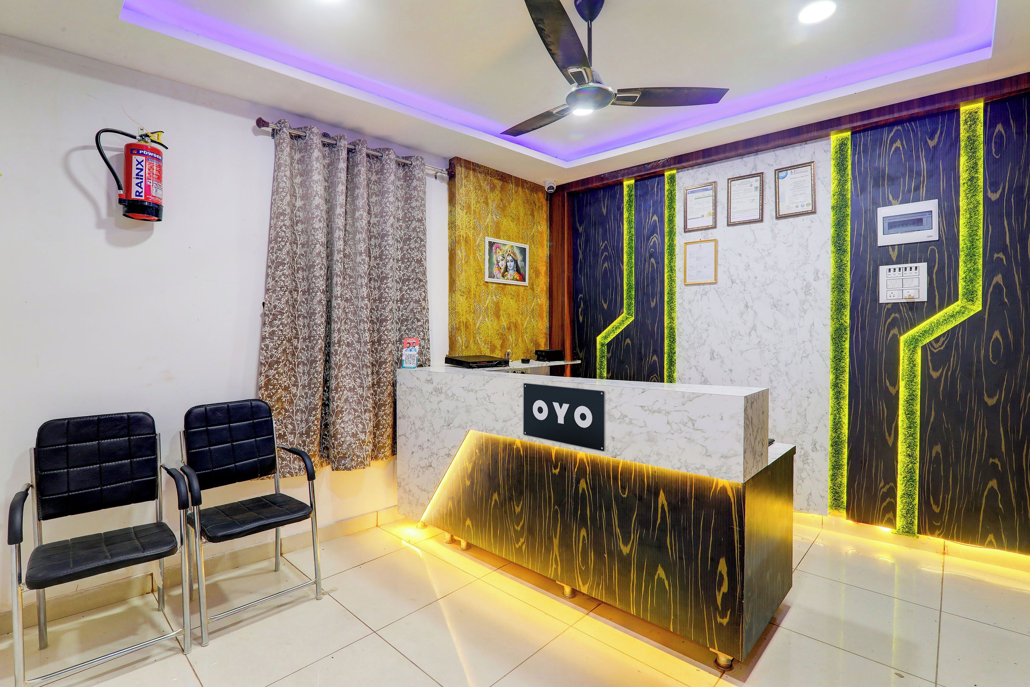 A reception area with a marble counter, two black chairs, a ceiling fan, and a fire extinguisher.