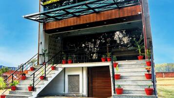 Un hotel con un letrero que indica habitaciones de lujo y un restaurante. Se observan escalones exteriores con plantas en macetas que conducen a la entrada.