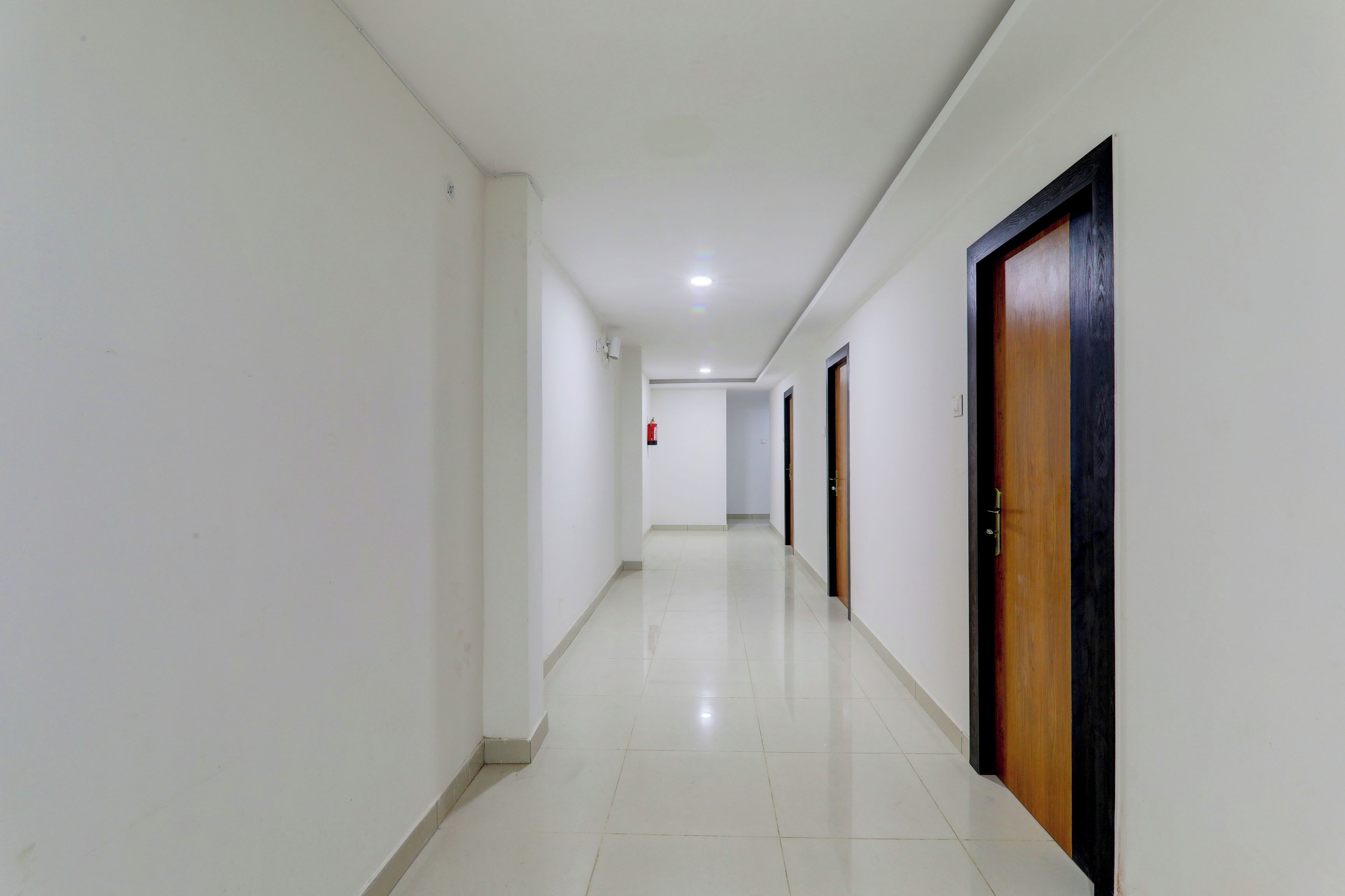 A corridor with white walls, a tiled floor, and doors with wooden frames.