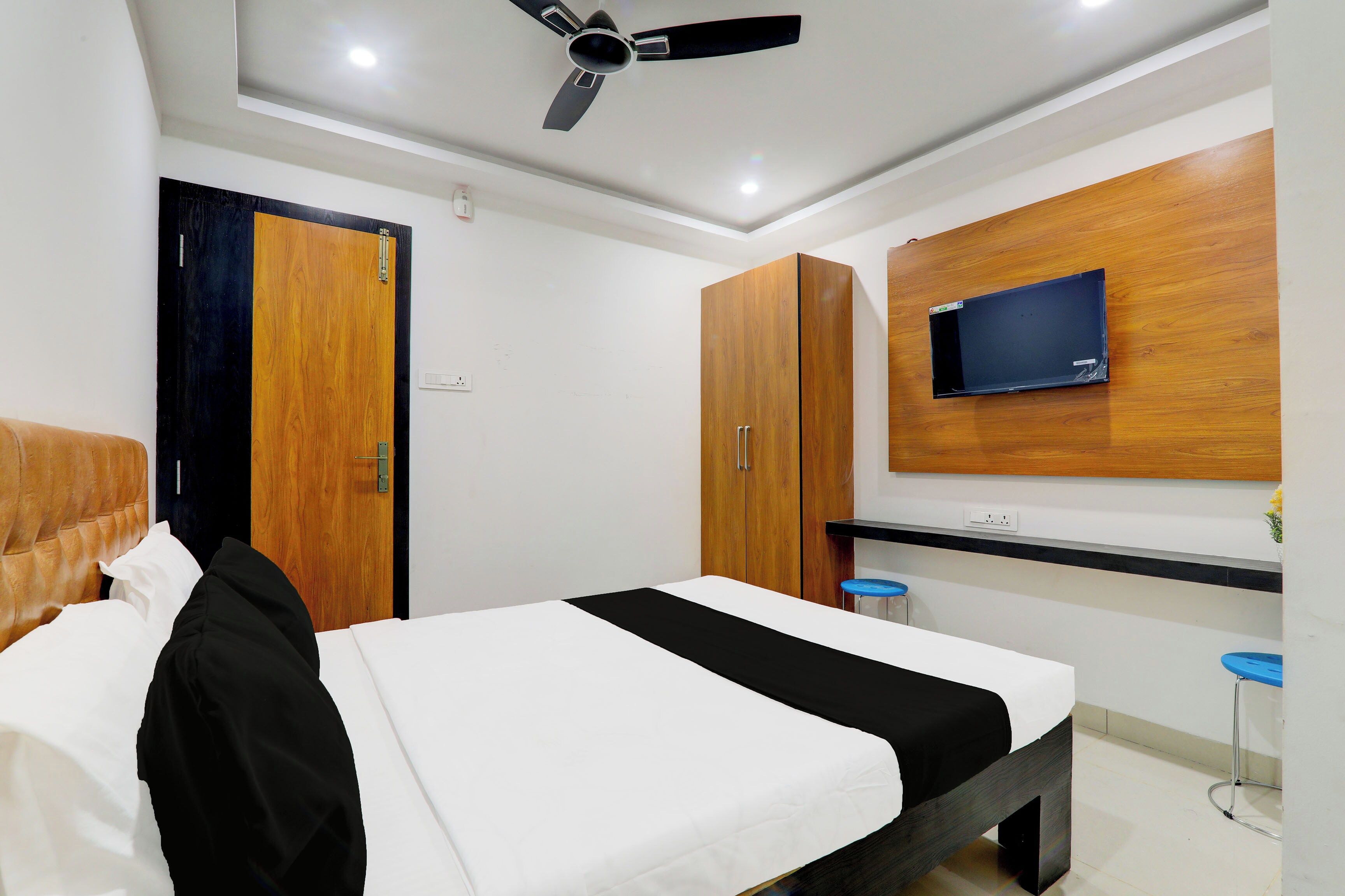 A bedroom with a bed, a desk, a TV mounted on the wall, and a ceiling fan.