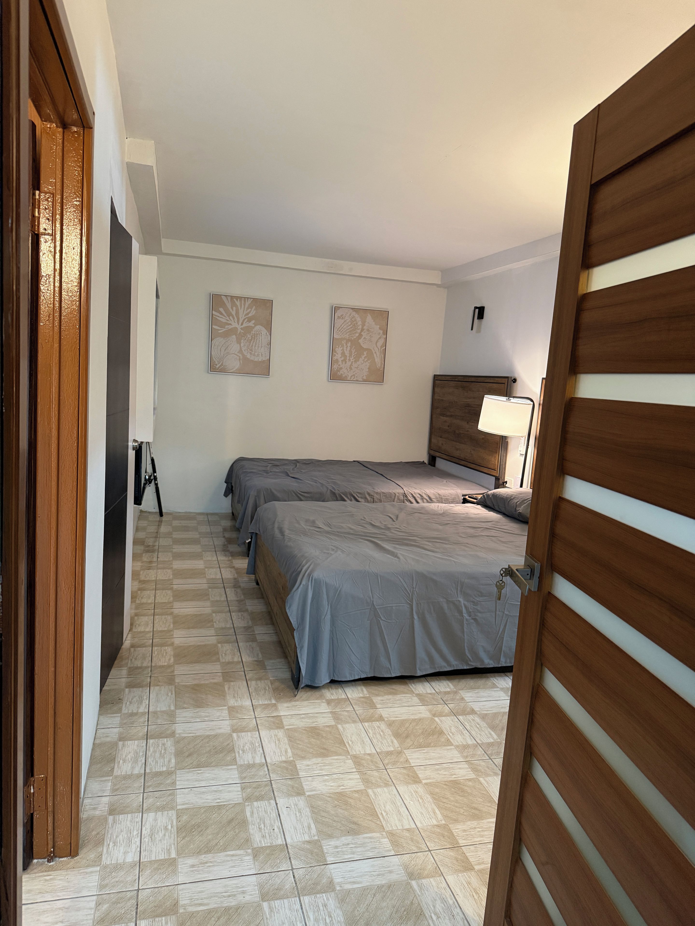 A hotel room with two beds, a wooden wardrobe, a standing lamp, and a check-in station.