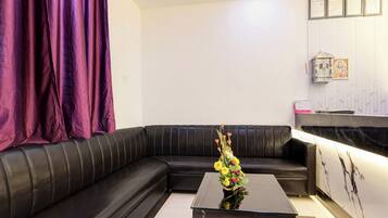 A modern living room with a black leather sofa, a glass coffee table, and a purple curtain.